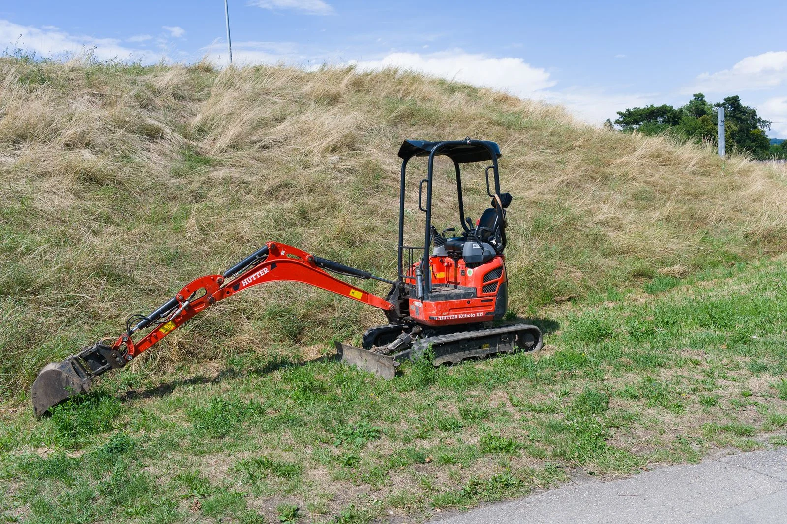 Miniexcavadora con el brazo extendido sobre un talud de hierba